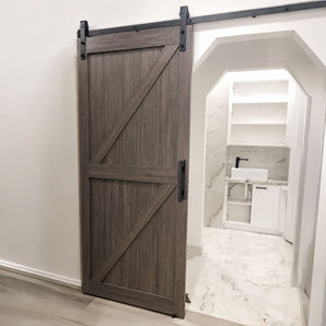 A dark brown wood sliding barn door with black metal hardware, shown partially open in a modern bathroom setting.