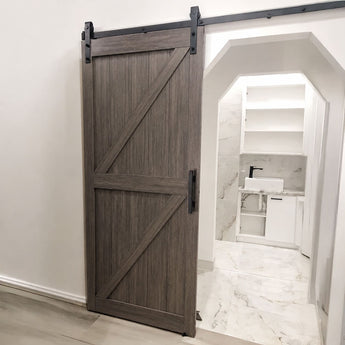 A dark brown wood sliding barn door with black metal hardware, shown partially open in a modern bathroom setting.
