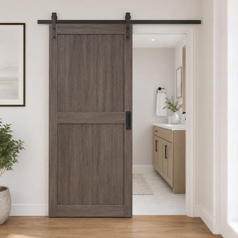 A dark brown wood sliding barn door with a black metal track and hardware, installed in a white hallway with a view into a bathroom.